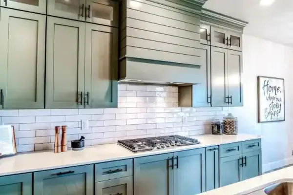 A modern kitchen features sage green cabinets, a white subway tile backsplash, and a built-in gas cooktop—showcasing beautiful flooring installation Wake County, NC and Horry County residents love. A framed sign hangs on the adjacent wall.