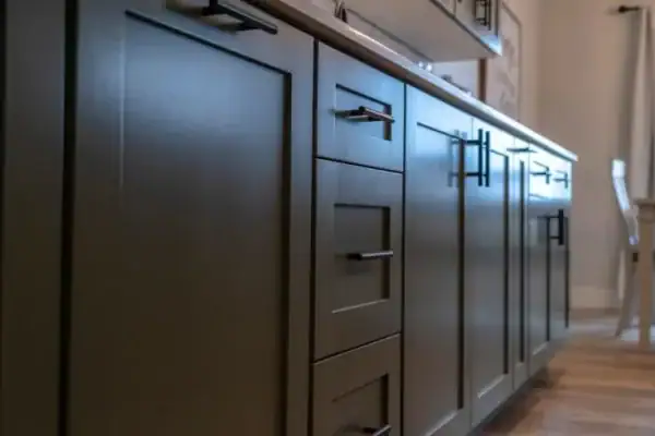 Laehoek-aansig van moderne kombuiskaste met donker handvatsels en 'n ligte houtvloer, wat kundige vloerinstallasie in Wake County, NC en Horry County ten toon stel—wat 'n ry laaie en kaste langs 'n skoon, kontemporêre toonbank uitlig.