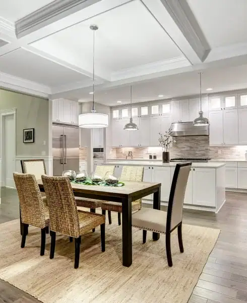 'n Moderne kombuis en eetkamer met wit kaste, vlekvrye staal toestelle, 'n donkerhout eetkamertafel, vier rietstoele, hanglampe en 'n ligkleurige mat op houtvloer – ideaal vir huise in NC en Horry County of na vloerinstallasie in Wake County, SC.