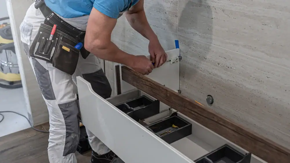 A person wearing a tool belt installs a drawer into a cabinet, using a screwdriver to secure the component—demonstrating the same attention to detail seen in Flooring Installation Wake County, NC and Horry County, SC.