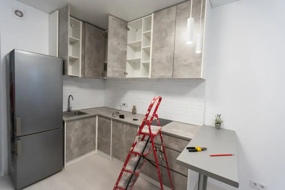 'n Moderne kombuis met grys kaste, sommige oop en leeg, 'n silwer yskas, 'n wasbak, 'n elektriese kookplaat, klein eetkamertafel, gereedskap en 'n rooi trapleertjie&mdash;ideaal vir vloerinstallasie in Wake County, NC of Horry County, SC.